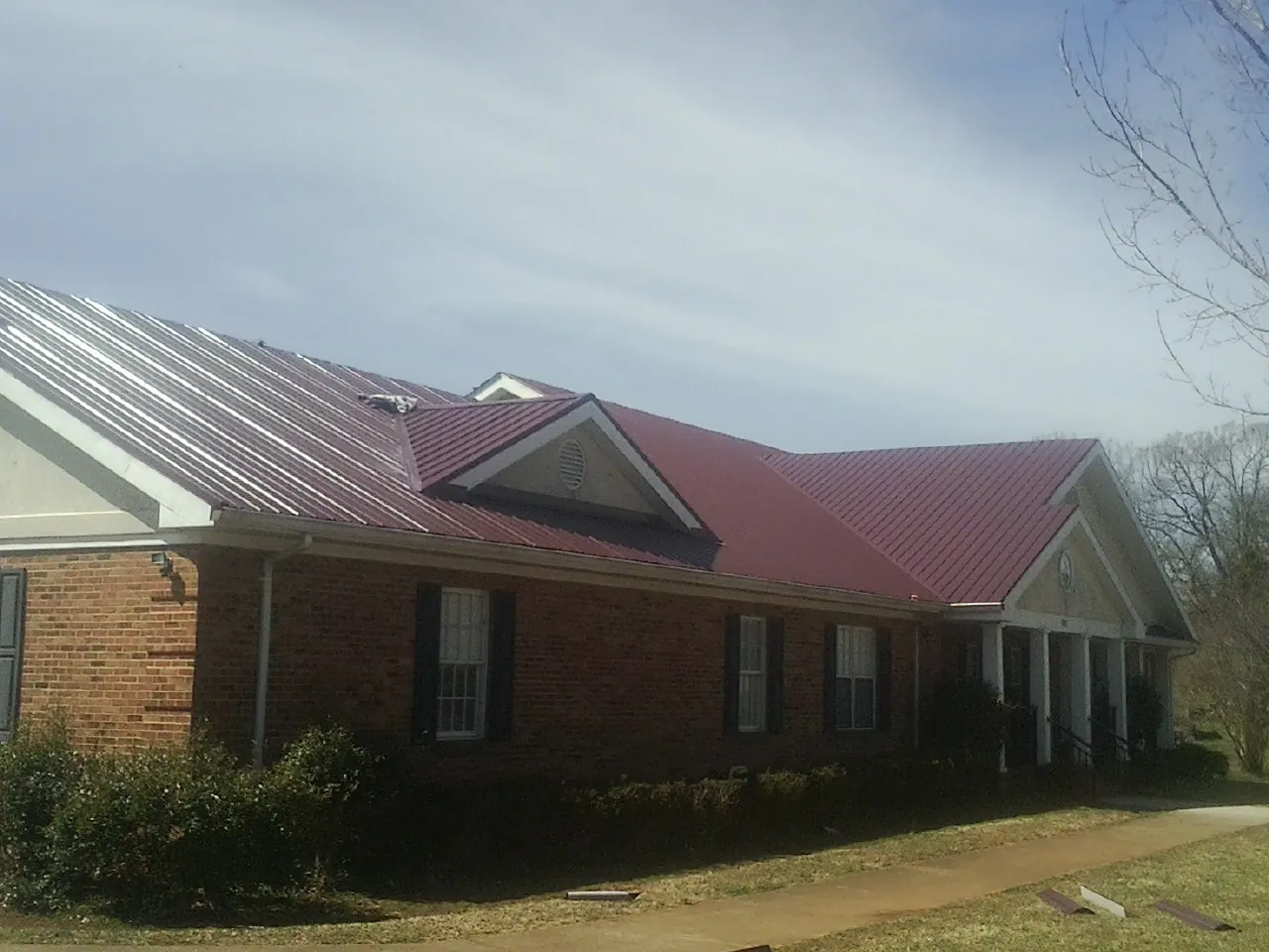 Red metal roof with gabled entries on a long brick building, from a Hail Damage Roof Repair job in Adel