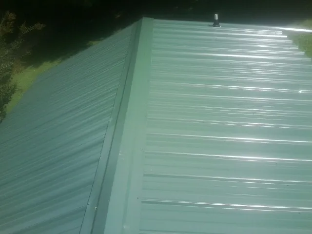 New green metal panels meeting at the ridge of a roof — Flat Roof Repair work by our crew in Adel