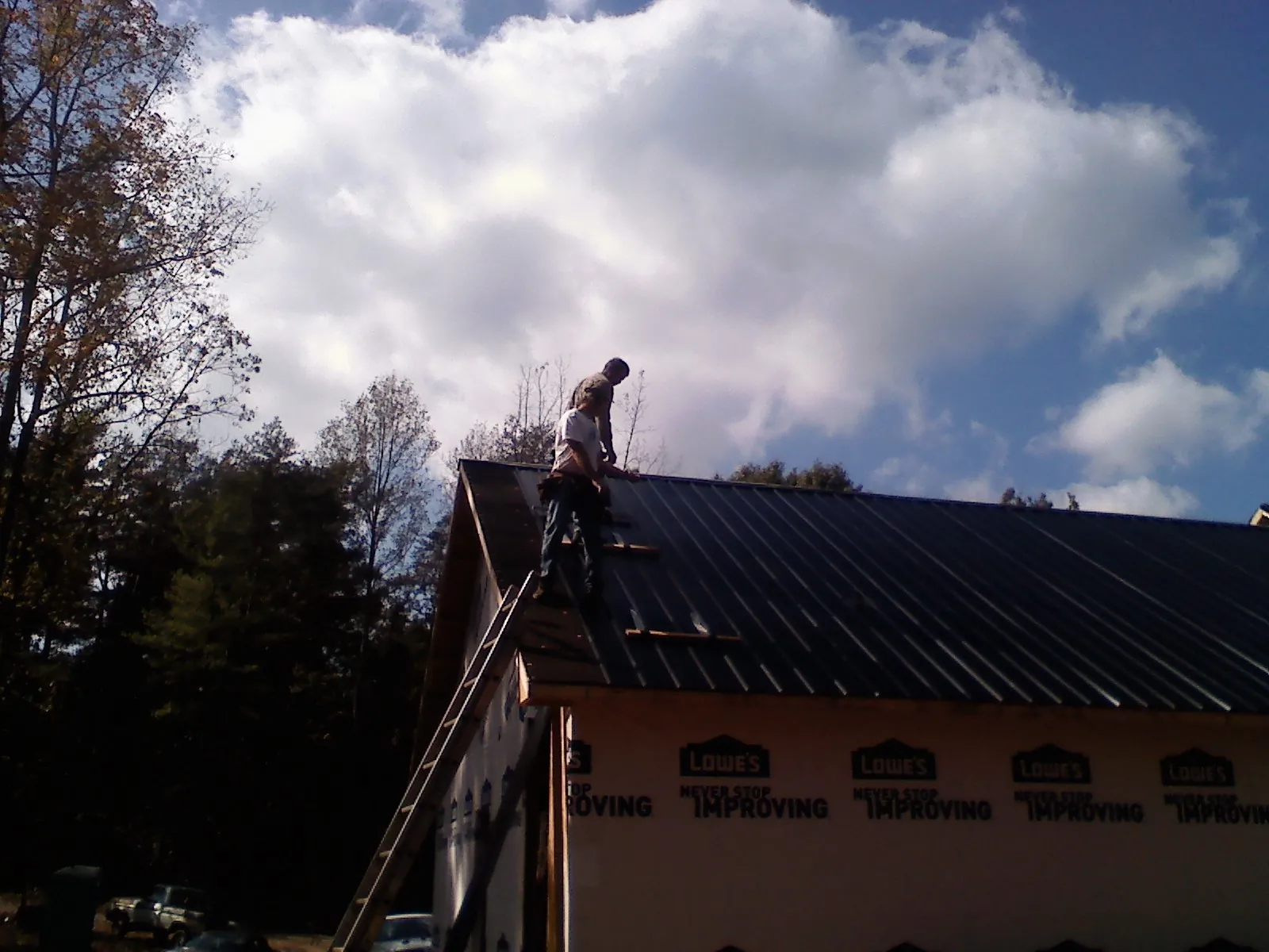 Roofer fastening dark metal panels high against a cloudy sky, from a Roof Inspection job in Adel