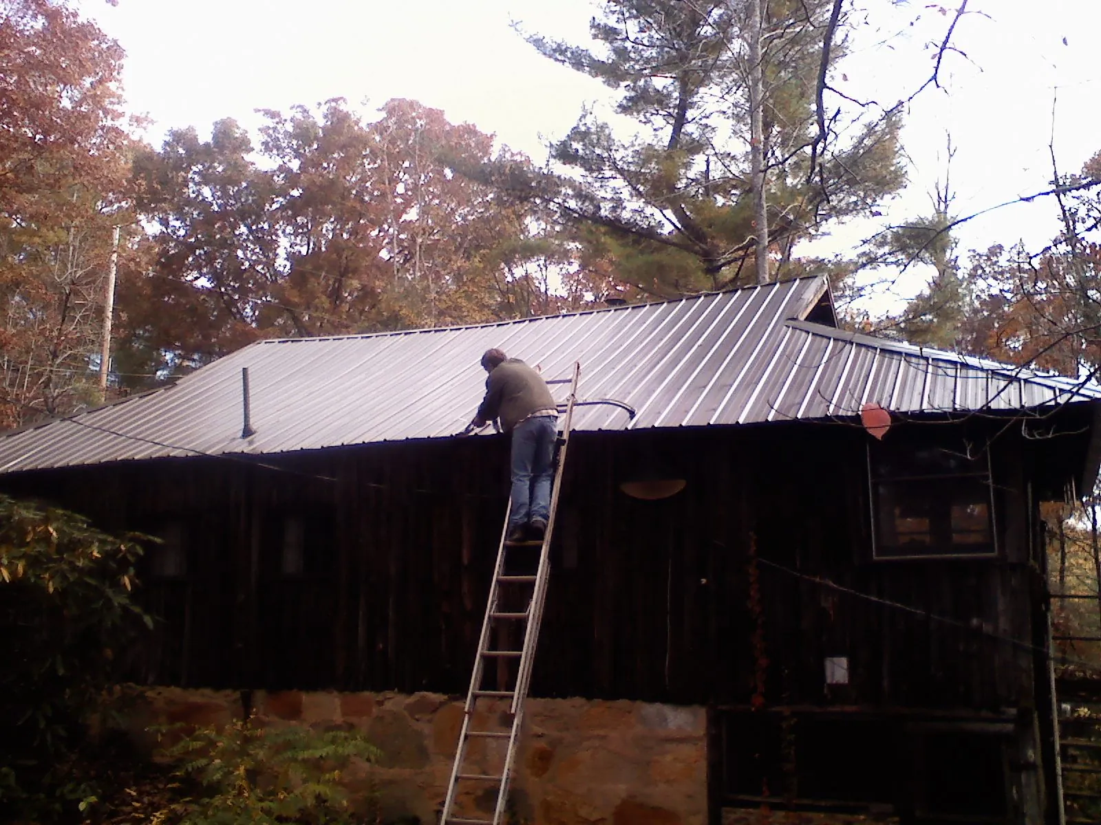 Roofer on a ladder working along the edge of a cabin metal roof in Adel
